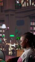 vertical menina empurrando dela colega com fisica imparidade através a biblioteca, estudando para uma Novo exame com acadêmico materiais a partir de a campus base de dados. africano americano aluna dentro cadeira de rodas. Câmera uma. video