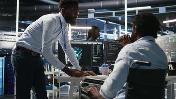 Vertical Server farm supervisor and man with disability adjust system settings based on AI analytics. Data center manager talking with technician in wheelchair overseeing automated node tree tool, camera A video