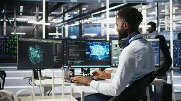 Vertical Data center system administrator using AI neural network models to configure hardware. Employee works on machine learning programming language in server room, optimizing system functionality, camera A video