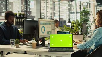 Green screen mockup laptop next to accountant inputting financial figures on PC after checking reports. Chroma key notebook next to businesswoman working in office, crosschecking data, camera B video