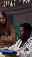 Vertical Multiethnic group of students in a library participate at a lesson with doctor, using medical books and materials to gain expertise in pharmacology and microbiology. Scientific studies. Camera B. video