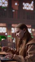Vertical Female student reading and writing detailed notes for an exam, studying political science for upcoming lecture in a library setting at the university. Young adult consults a colleague. Camera B. video