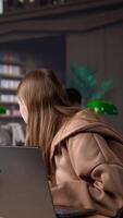 Vertical Young scholar focuses on exam preparations in the campus library with colleague, takes notes on laptop from reference books in a peaceful study setting. Girl uses the database materials. Camera B. video
