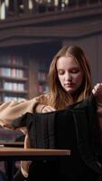 Vertical Focused girl arriving at university library and opening textbook to write notes, doing research with the help of massive books database at campus designated space for self learning. Camera A. video