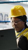 Vertical Woman conducts routine inspections in industry 4.0 solar panels plant using laptop. Engineer in photovoltaics smart factory testing equipment and reviewing system metrics using notebook video