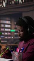 Vertical Male student listening to ambient study music on headset and collecting data from a book, focusing on school projects. Enjoying focus ambience music to finish a school assignment. Camera B. video