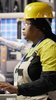 Vertical Portrait of cheerful factory engineer typing on PC, overseeing monitoring of production lines. Jolly woman in industry 4.0 plant ensuring machinery operates at optimal efficiency, camera B video