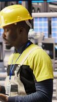 Vertical Technician in industrial plant using tablet app to diagnose equipment errors. Manufacturing factory specialist using digital device to coordinate repair tasks on assembly lines, camera A video