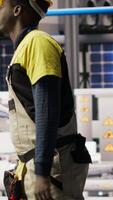 Vertical Engineer walking in smart solar manufacturing facility, using toolbox to calibrate high tech machinery. African american man troubleshooting photovoltaic assembly equipment, camera B video