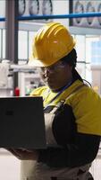 Vertical Portrait of smiling solar panels factory engineer analyzing data on laptop to predict gear failures. Happy photovoltaics plant employee using notebook, following maintenance procedures, camera A video