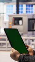 Vertical Close up of green screen tablet used by engineer in factory to perform maintenance, analyzing IoT sensors data. Industrial plant worker managing photovoltaic systems using chroma key device, camera A video