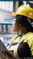 Vertical Smiling engineer in smart factory performing predictive maintenance using tablet, analyzing IoT sensor data. Industrial plant worker managing operational reliability of photovoltaic systems, camera B video
