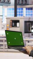 Vertical Technician in industrial plant using green screen laptop to diagnose equipment errors. Factory specialist using chroma key mockup notebook to coordinate repair tasks on assembly lines, camera A video