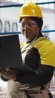 Vertical Solar panels plant technician uses laptop to oversee systems, ensuring machinery operates at optimal efficiency. Photovoltaics plant employee uses software on notebook to maintain operations, camera A video