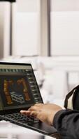 Vertical Technician in sustainable industrial plant monitors production equipment using laptop, diagnosing malfunctions. Factory worker coordinates repair tasks on solar module assembly line, camera A close up video