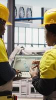 Vertical Smart solar panels factory engineering team using laptop to oversee production lines. Teamworking industry 4.0 plant coworkers ensure machinery operates at optimal efficiency using notebook, camera A video