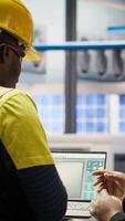 Vertical Smart solar panels factory engineering team using laptop to oversee production lines. Teamworking industry 4.0 plant coworkers ensure machinery operates at optimal efficiency using notebook, camera B video
