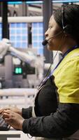 Vertical Call center agent in smart factory using headset to assist remotely with maintenance queries, monitoring automated solar panel assembly processes, providing technical guidance, camera A video