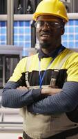 Vertical Portrait of technician overseeing solar panel production lines equipment. African American man maintaining photovoltaic assembly systems in automated industry 4.0 factory using computer, camera A video