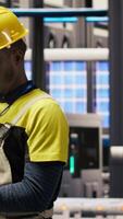 Vertical Technician in smart factory using notebook to look at system performance metrics. African american man in industry 4.0 plant using laptop to track energy production through IoT sensors, camera B video