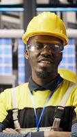 Vertical Portrait of technician overseeing solar panel production lines equipment. African American man maintaining photovoltaic assembly systems in automated industry 4.0 factory using computer, camera B video