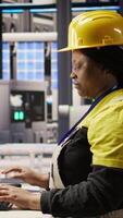 Vertical Woman in smart factory expert uses computer to implement automated workflows. African american technician using PC in industry 4.0 plant to integrate sensors into production, camera A video