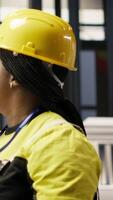 Vertical Woman in smart factory expert uses computer to implement automated workflows. African american technician using PC in industry 4.0 plant to integrate sensors into production, camera B video