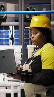 Vertical Engineer walking in smart factory, using laptop to analyze IoT sensors data, refining gear efficiency. Industry 4.0 plant expert performing system diagnostics to reduce downtime, camera A video