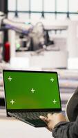Vertical Technician in industrial plant using green screen laptop to diagnose equipment errors. Factory specialist using chroma key mockup notebook to coordinate repair tasks on assembly lines, camera B video