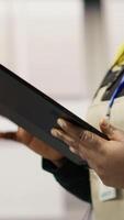 Vertical Engineer in smart factory oversees robotic assembly lines using tablet app, ensuring quality control during manufacturing. Worker monitoring automated conveyor systems using device, camera B close up video