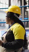 Vertical Smart solar panels factory engineer using tablet to oversee production lines. Woman in industry 4.0 photovoltaics plant ensures machinery operates at optimal efficiency using device, camera A video
