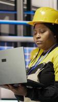 Vertical Engineer walking in smart factory, using laptop to analyze IoT sensors data, refining gear efficiency. Industry 4.0 plant expert performing system diagnostics to reduce downtime, camera B video