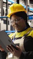 Vertical Upbeat professional working in smart factory oversees robot production lines, ensuring quality control. Industry 4.0 plant expert monitoring automated conveyor systems using notebook, camera A video