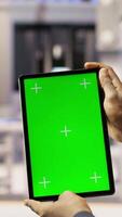 Vertical Engineer in smart factory oversees robotic assembly lines using green screen tablet, ensuring quality control. Worker monitoring automated conveyor systems using chroma key device, camera B closeup video