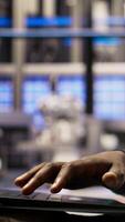 Vertical Engineer in smart factory oversees robotic assembly lines using laptop software, ensuring quality control. Worker monitoring automated conveyor systems using notebook program, camera A closeup video