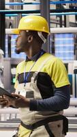Vertical Smart factory mechanic using tablet to analyze IoT sensors data before modifying gear. African american man in industry 4.0 plant performing system diagnostics to reduce downtime, camera A video