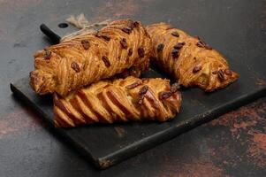 golden brown maple pecan braid pastries are arranged on a dark, textured surface. Braided dough is flaky and topped with pecans. photo