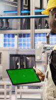 Vertical Engineer in smart factory oversees robotic assembly lines using green screen tablet, ensuring quality control. Worker monitoring automated conveyor systems using chroma key device, camera A closeup video