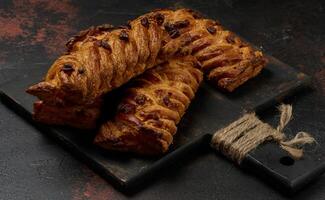 Golden brown maple pecan braid pastries are arranged on a dark, textured surface. Braided dough is flaky and topped with pecans photo