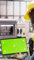 Vertical Engineer in smart factory using green screen laptop to analyze IoT sensors data. Industry 4.0 plant expert performing system diagnostics on chroma key mockup notebook to reduce downtime, camera B video