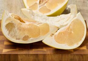 A fresh, juicy slice of pomelo fruit with visible pulp and peel. Citrus fruit section on wooden table photo