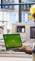 Vertical Engineer in smart factory using green screen laptop to analyze IoT sensors data. Industry 4.0 plant expert performing system diagnostics on chroma key mockup notebook to reduce downtime, camera A video