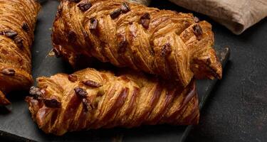 Three golden brown maple pecan braid pastries are arranged on a dark, textured surface. Braided dough is flaky and topped with pecans photo
