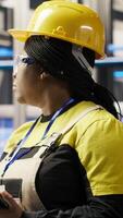 Vertical Smart solar panels factory engineer using tablet to oversee production lines. Woman in industry 4.0 photovoltaics plant ensures machinery operates at optimal efficiency using device, camera B video