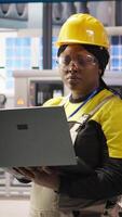 Vertical Engineer performing predictive maintenance using laptop, analyzing IoT sensor data, managing operational reliability of photovoltaic systems in smart factory environment, camera A video