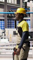 Vertical Engineer walking in smart solar manufacturing facility, using toolbox to calibrate high tech machinery. African american man troubleshooting photovoltaic assembly equipment, camera A video