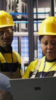 Vertical Smart factory engineering team using laptop to calibrate high tech machinery and analyze sensor data. Teamworking colleagues at work troubleshooting assembly equipment, camera A video
