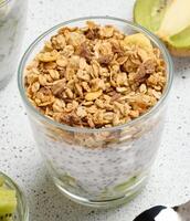 Glass filled with chia seed pudding, layered with diced kiwi at the bottom and topped with crunchy granola. photo