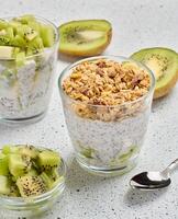 Glass filled with chia seed pudding, layered with diced kiwi at the bottom and topped with crunchy granola photo