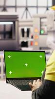Vertical Factory engineer typing on green screen laptop, monitoring production lines. Woman in industry 4.0 plant ensures machinery operates at optimal efficiency using chroma key mockup notebook, camera B video